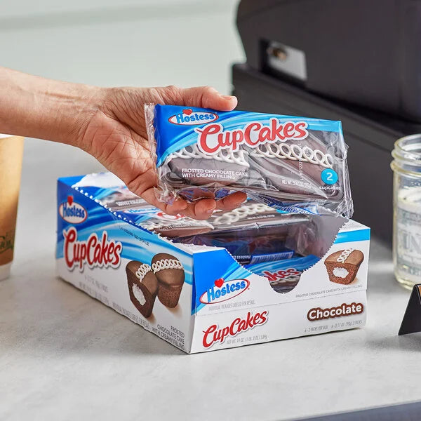 A vibrant display of assorted Hostess CupCakes, including classic chocolate with white squiggles, golden vanilla, and pink strawberry, on a colorful background.